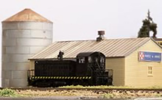 An N-scale model town with weathered buildings and tall, uncut grass.